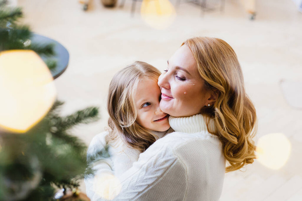 A girl with her mother near the Christmas tree, the interior decorated for the new year and Christmas, family and joy, traditions - Photo, Image