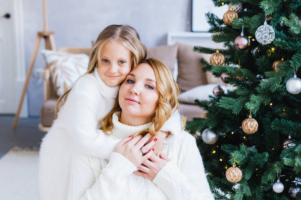 A girl with her mother near the Christmas tree, the interior decorated for the new year and Christmas, family and joy, traditions - Valokuva, kuva