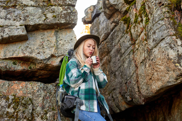 charming blonde female is drinking hot tea during hiking - 写真・画像