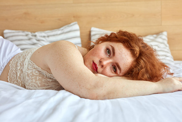 İç çamaşırlı, kızıl saçlı tombul kadın yatağa uzanıp dinleniyor. - Fotoğraf, Görsel