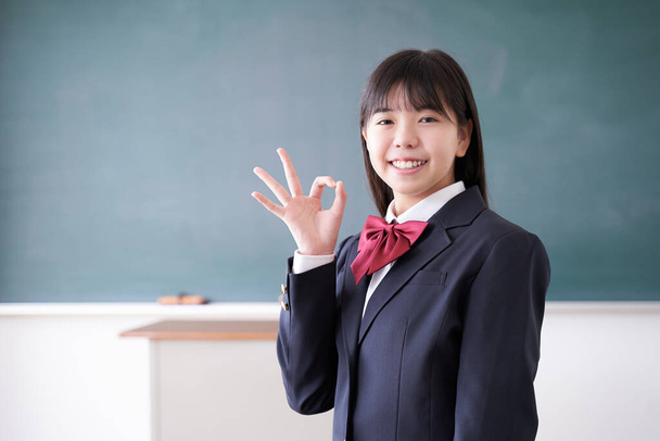 Uma menina japonesa do ensino médio júnior faz uma pose OK na sala de aula. - Foto, Imagem