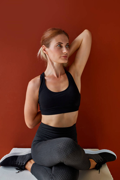 slim female in sportswear stretching legs and arms sitting on box - Fotografie, Obrázek