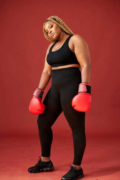 portrait of confident fat afro american woman standing with boxing gloves in fighting pose - 写真・画像