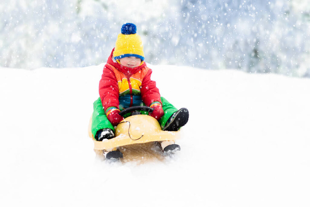 小さな男の子がそりに乗るのを楽しんでいる。子供のそり。幼児はそりに乗っている。子供たちは雪の中屋外で遊ぶ。冬にはアルプスの山々で子供たちがそります。家族のための屋外の楽しみクリスマス休暇. - 写真・画像