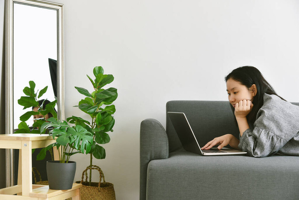 Kobieta pracująca z domu przez laptop komputer otaczają zielone tropikalne drzewo, Człowiek i natura, Rośliny domowe rosnące w salonie do oczyszczania powietrza wewnątrz i dekoracyjne domu. - Zdjęcie, obraz