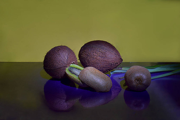 Pokrojone i całe kiwi, kokosy na wypolerowanym fioletowym stole, zbliżenie. - Zdjęcie, obraz