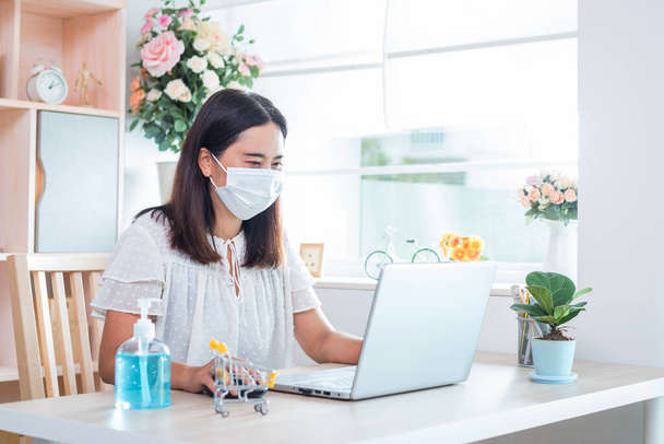 The woman wearing a mask currently working at home and shopping online for self quarantine during the outbreak Corona virus Disease (COVID-19). - Photo, Image