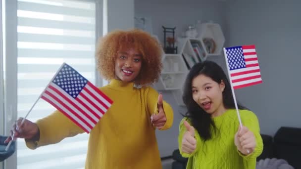 Multiraciální přátelství a výměnný program studentů. Africká americká a asijská žena drží vlajky USA s palci nahoru  - Záběry, video