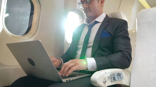 Genç işadamı uçakta dizüstü bilgisayar kullanıyor. - Fotoğraf, Görsel
