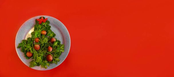 Christmas tree made of herbs and hazelnuts on a plate. New year decor from food. Isolated on a red background. Copy space - 写真・画像