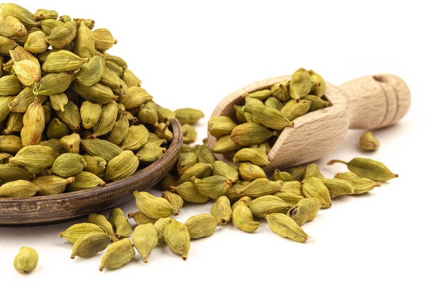 Isolated cardamom seeds in wooden plate and scoop - Photo, Image