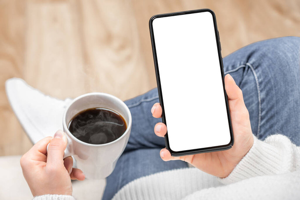 Mockup image of a woman holding and using black mobile phone with blank desktop screen while drinking coffee in cafe. woman's hand holding white mobile phone with blank desktop screen and coffee cup. - Photo, image