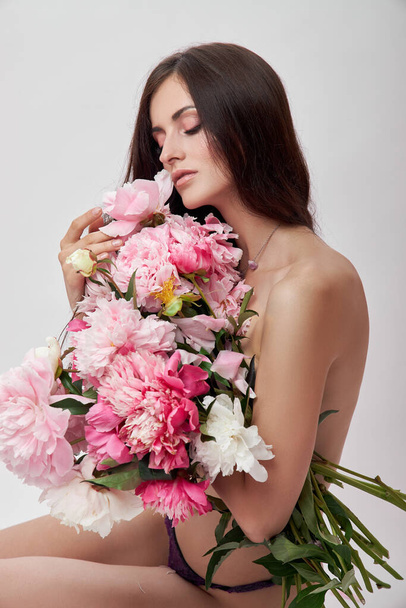 Beautiful woman with lots of pink flowers in her hands. Sexy woman with long hair - Фото, зображення