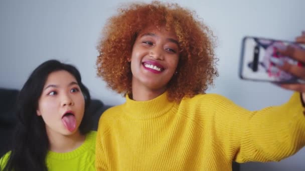 Asyalı ve Afrikalı Amerikalı siyahi kadınlar akıllı telefon kullanarak selfie çekiyorlar. Komik yüzler. - Video, Çekim