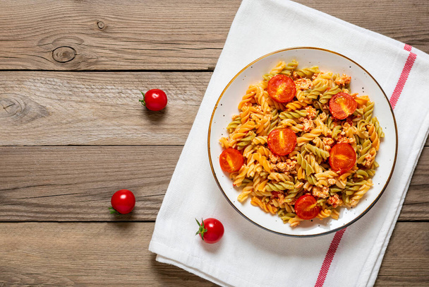 Fusili -伝統的なイタリアのパスタデュラム小麦から鶏肉,トマトチェリー,木製のテーブルの上に白いボウルにトマトソースのバジル地中海料理トップビューフラットレイ - 写真・画像