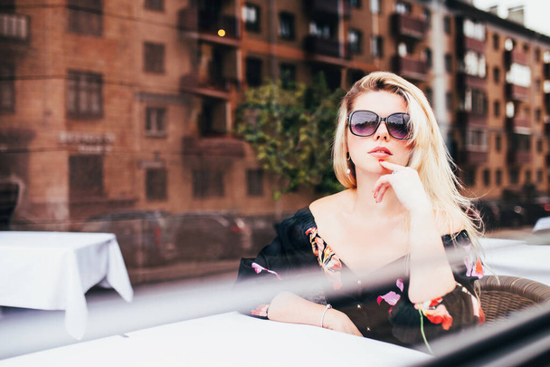 A charming blonde woman with a figure attracts the attention of men at a cafe table - Фото, зображення