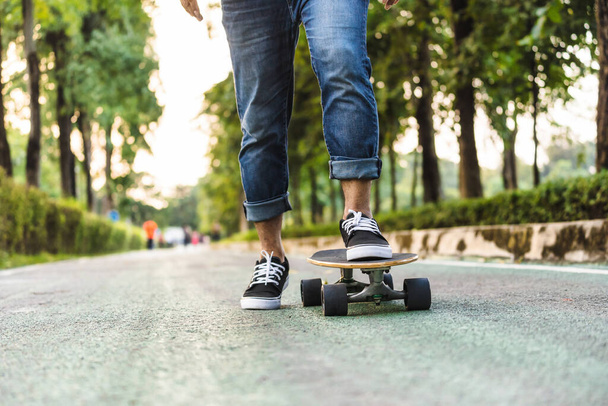 Closeup Asian man legs on surfskate or skate board in outdoor Park when sunrise time over photo blur of unrecognized people running, extream sport, healthy and exercise, fashion in covid19 concept - Foto, Imagem