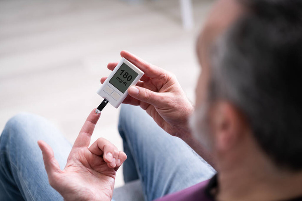 Elderly Man Using Glucometer To Check Blood Sugar Level At Home - Foto, Imagen