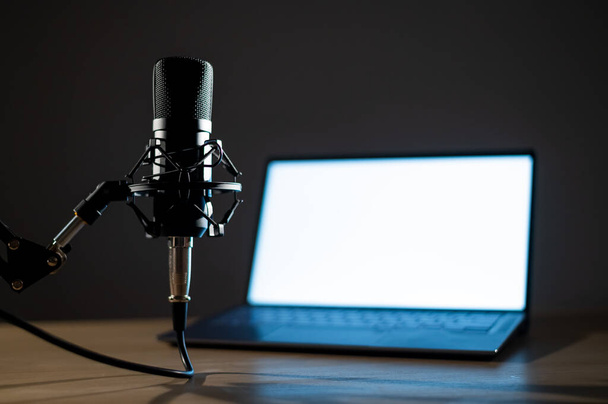 Professional microphone and laptop with white screen in the dark. Equipment in a recording and broadcasting studio - Φωτογραφία, εικόνα