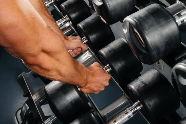 An athlete takes dumbbells from racks in the gym, close-up. Fitness, bodybuilding - Foto, afbeelding