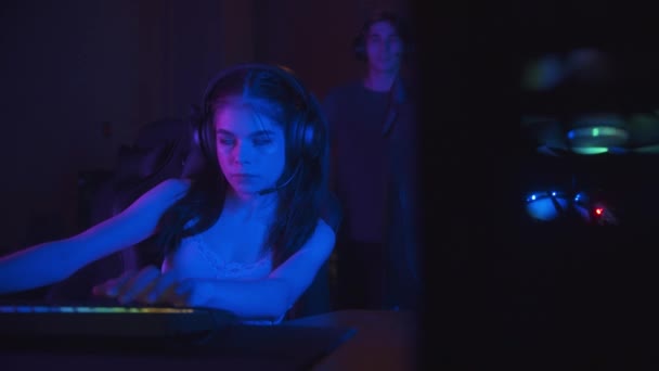 Zwei Mädchen spielen ein Online-Spiel im Neon-Gaming-Club - ihre Freundin kommt zu ihnen und beginnt zu reden - Filmmaterial, Video