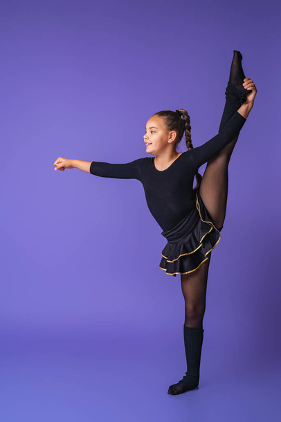 Young gymnast girl doing an exercise on purple background studio. childrens professional sports. child does stretching. children's professional sports. Cheerleading/ Copy space. - Zdjęcie, obraz