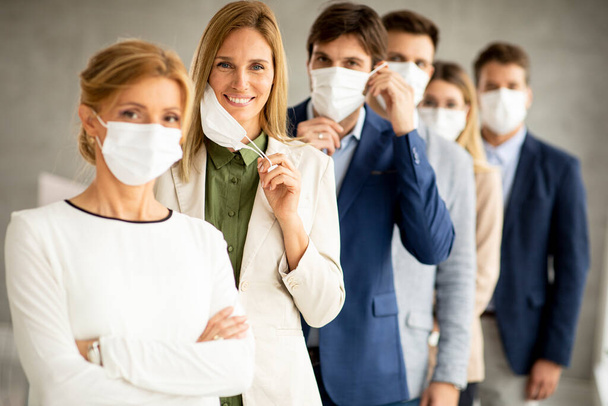 Business woman taking off her protective facial mask and looking at the camera with her team members standing in the line at the office - Photo, Image