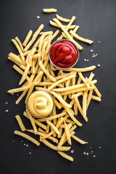 French fries on black board with ketchup and cheese sauce, top view, copy space. Homemade french fries. - 写真・画像