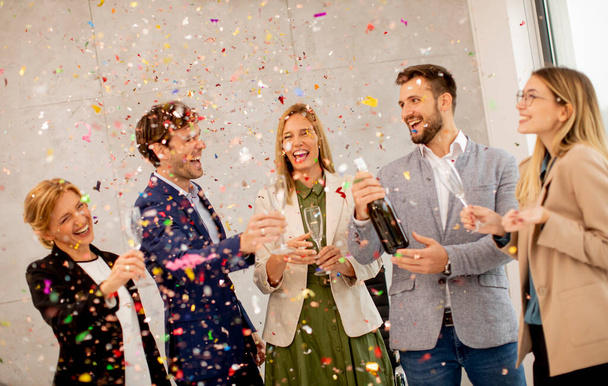 Gruppe aufgeregter Geschäftsleute feiert und stößt im Büro mit Konfetti an - Foto, Bild