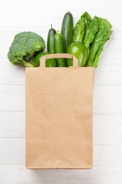 Verschiedene grüne gesunde Lebensmittel in Recycling-Papiertüten auf einem Holztisch. Eco-Food-Konzept. Draufsicht flach lag mit Kopierraum - Foto, Bild
