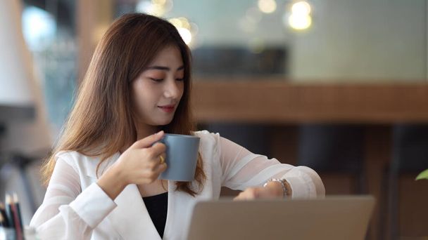 Portrait of female office worker take a coffee break and looking on wristwatch while working in office - 写真・画像