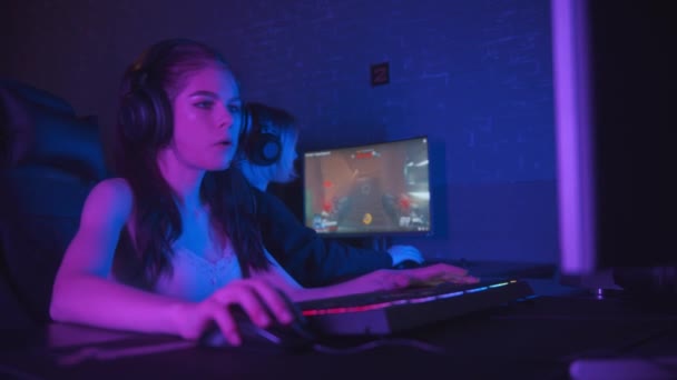 Δύο όμορφα κορίτσια gamer παίζει ένα online παιχνίδι shooter στο σκοτεινό νέον gaming club - Πλάνα, βίντεο