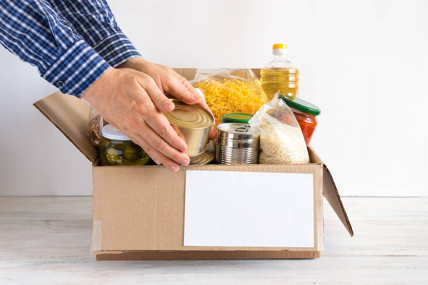 Cardboard box with butter, canned food, cereals and pasta. A donation box with various food items. The hands are placed food. - Foto, afbeelding
