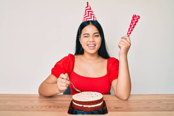 Joven chica asiática celebrando cumpleaños con pastel guiño mirando a la cámara con expresión sexy, cara alegre y feliz.  - Foto, imagen