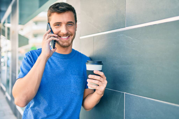 Fiatal kaukázusi férfi beszél az okostelefonon és iszik kávét a városban.. - Fotó, kép