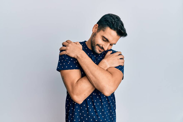 Young hispanic man wearing casual clothes hugging oneself happy and positive, smiling confident. self love and self care  - Photo, Image