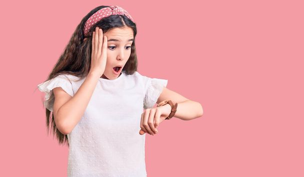 Χαριτωμένο κορίτσι ισπανόφωνη φορώντας casual λευκό μπλουζάκι κοιτάζοντας την ώρα ρολόι ανησυχούν, φοβούνται να πάρει αργά  - Φωτογραφία, εικόνα