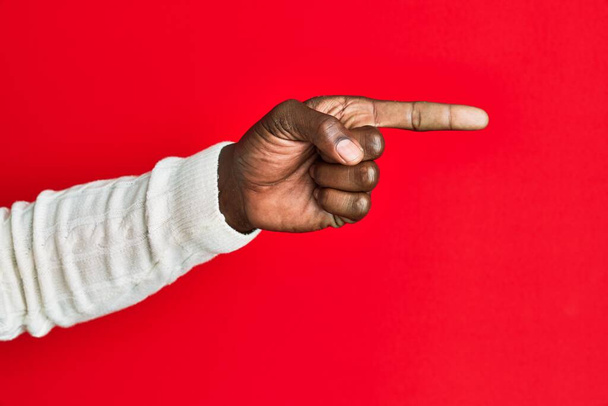 Arm ja käsi Afrikkalainen amerikkalainen nuori mies yli punainen eristetty tausta osoittaa etusormella sivulle, ehdottaa ja valitsemalla valinta  - Valokuva, kuva