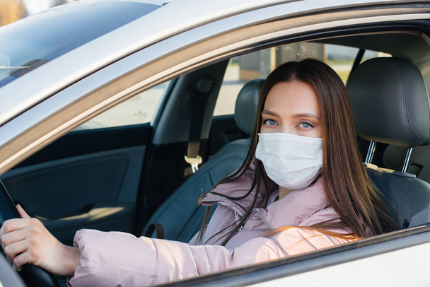 A young girl sits behind the wheel in the car in the mask during the global pandemic and coronavirus. Quarantine - Foto, Imagem