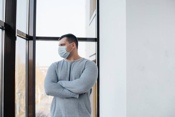 Un giovane uomo sta su uno sfondo grigio indossando una maschera durante una quarantena con spazio libero. Quarantena nella maschera - Foto, immagini