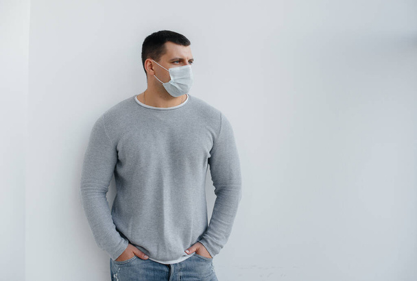 Een jongeman staat op een grijze achtergrond met een masker tijdens een quarantaine met vrije ruimte. Quarantaine in het masker - Foto, afbeelding