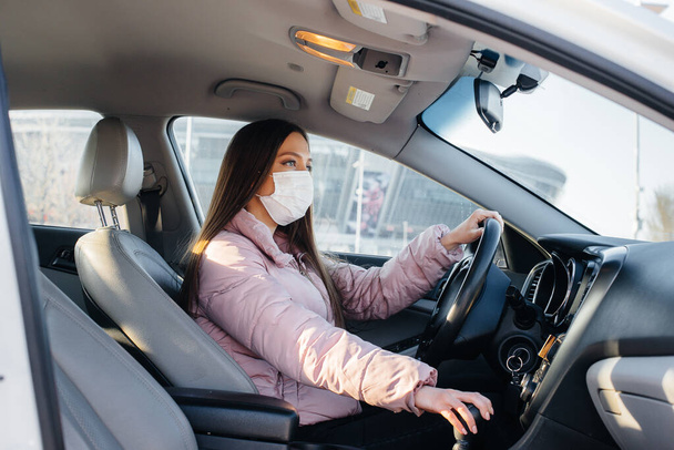 A young girl sits behind the wheel in the car in the mask during the global pandemic and coronavirus. Quarantine - Photo, image