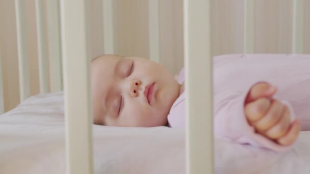 Sevimli küçük bebek tatlı bir şekilde beşiğinde uyuyor ve uyurken renkli rüyalar görüyor.. - Video, Çekim