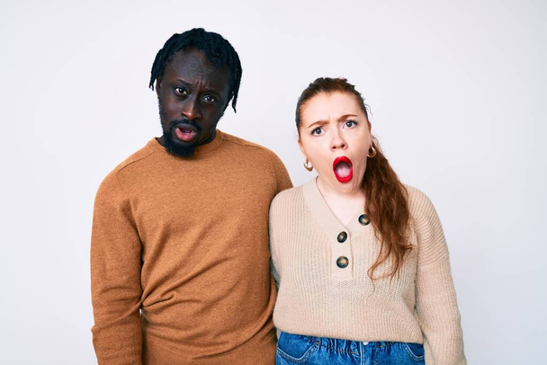Interracial couple wearing casual clothes in shock face, looking skeptical and sarcastic, surprised with open mouth  - Foto, Imagem