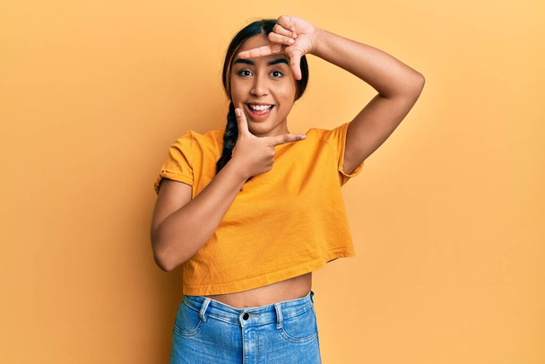 Young latin woman wearing casual clothes smiling making frame with hands and fingers with happy face. creativity and photography concept.  - Photo, Image