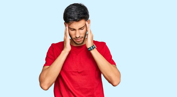 Mladý pohledný muž v neformálním červeném tričku s rukou na hlavě, bolest hlavy kvůli stresu. trpící migréna.  - Fotografie, Obrázek