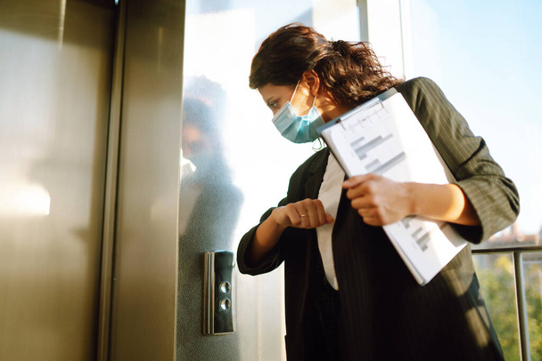 Business woman  in protective sterile mask use elbows to press elevator button to avoid using hands at modern office. Covid - 19. - Foto, imagen