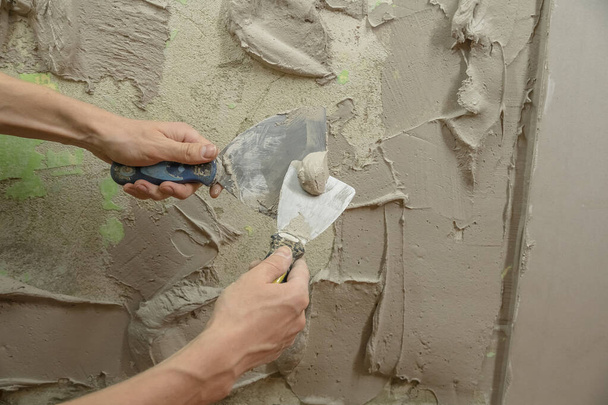 A worker plasters the wall with a spatula and applies a cement mix solution. The repairman lays the plaster on the drywall. Handyman repairs home. Laborer restore dwelling. Specialist covers up cracks - Photo, Image