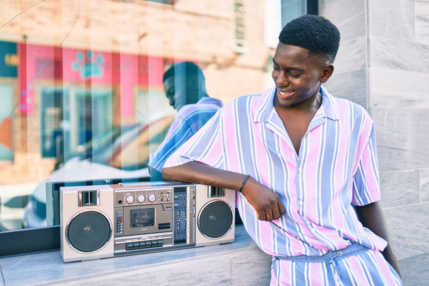 Young african american man listening to music using boom box leaning on the wall. - Photo, Image
