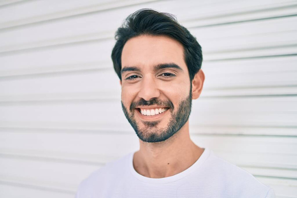 Молодий іспаномовний чоловік посміхається щасливим нахилившись на стіну в місті
. - Фото, зображення